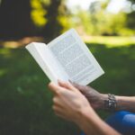 mãos de uma pessoa segurando livro cristão em um jardim verde